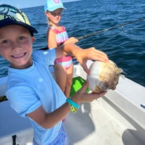 2 kids on a boat, 1 holds a fish